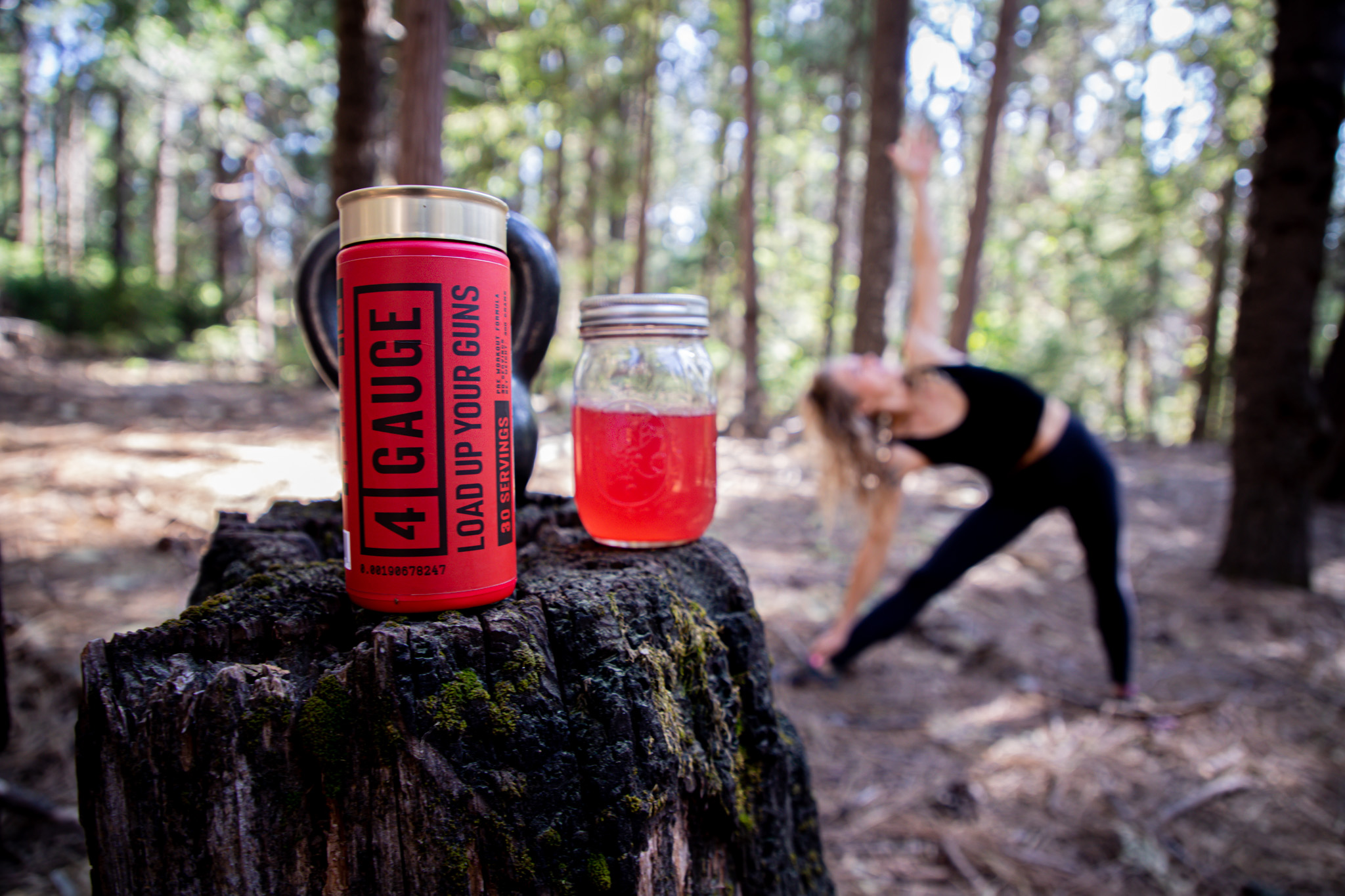 Woman doing exercise in a forest with a drink of 4Gauage in front of her