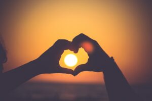A person wrapping their hands in a heart shape around the sun 