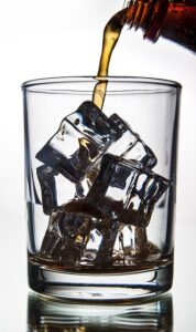 Soda is pouring into a glass with ice cubes 