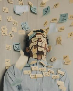 A man stands against a wall with post-it notes all over his face saying Take a Break