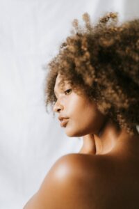 A woman stands with her back to the camera, shot from the side, with her natural brown hair